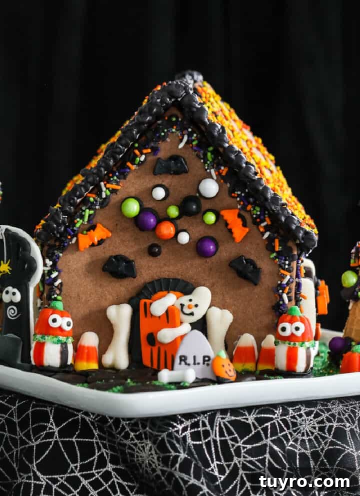 A Halloween gingerbread house decorated with royal icing and candy in orange, black, and white candy with a ghost opening the front door.