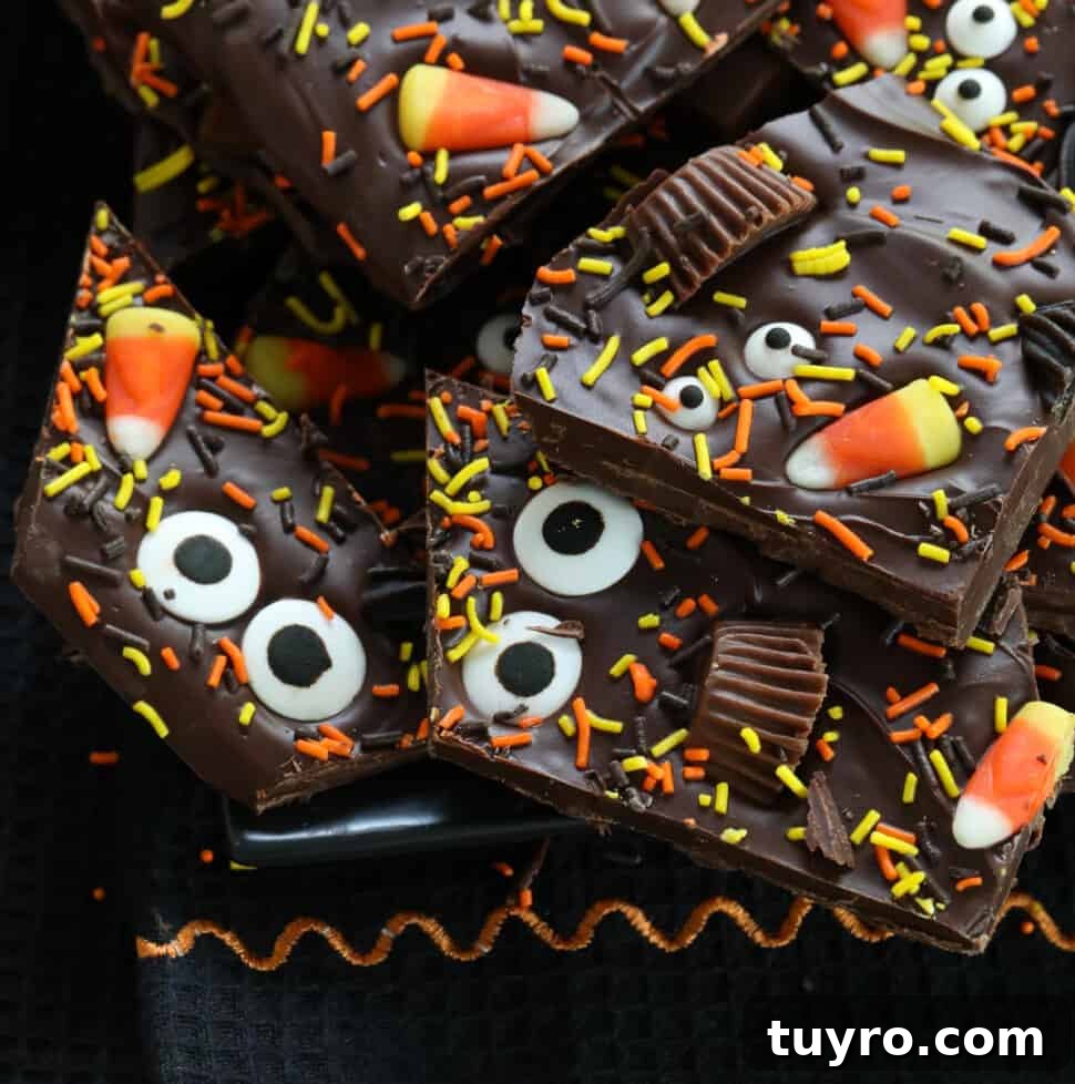 A pile of Halloween bark on a dark black platter decorated with candy and sprinkles.