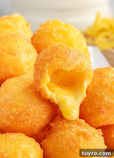 A pile of Fried Cheese Balls with one opened on the top to show the melted cheese.