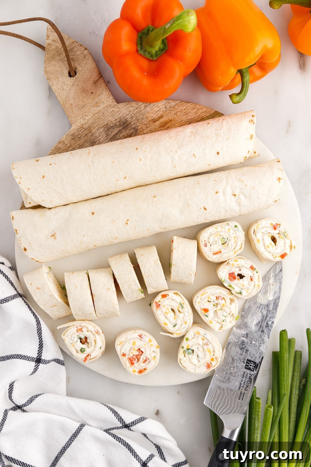 Creamy Ranch Pinwheel Appetizers for Parties and Potlucks 8 Top view of ranch pinwheels, part still rolled and others already sliced next to peppers and onions.