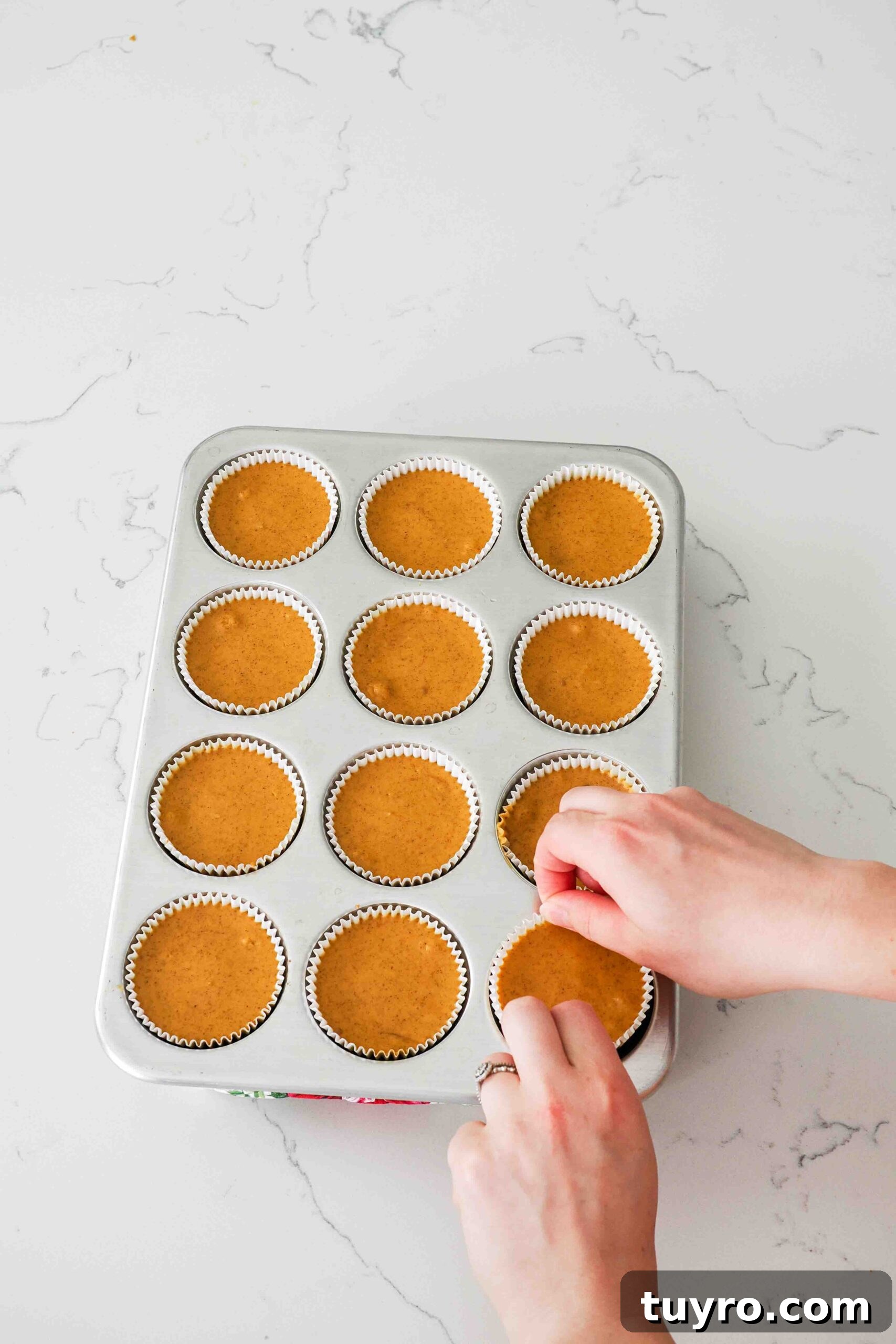 Mini Pumpkin Cheesecake Bites with Spiced Gingersnap Crust 14 Two hands pinch the liner of a mini cheesecake to remove it from a muffin pan.