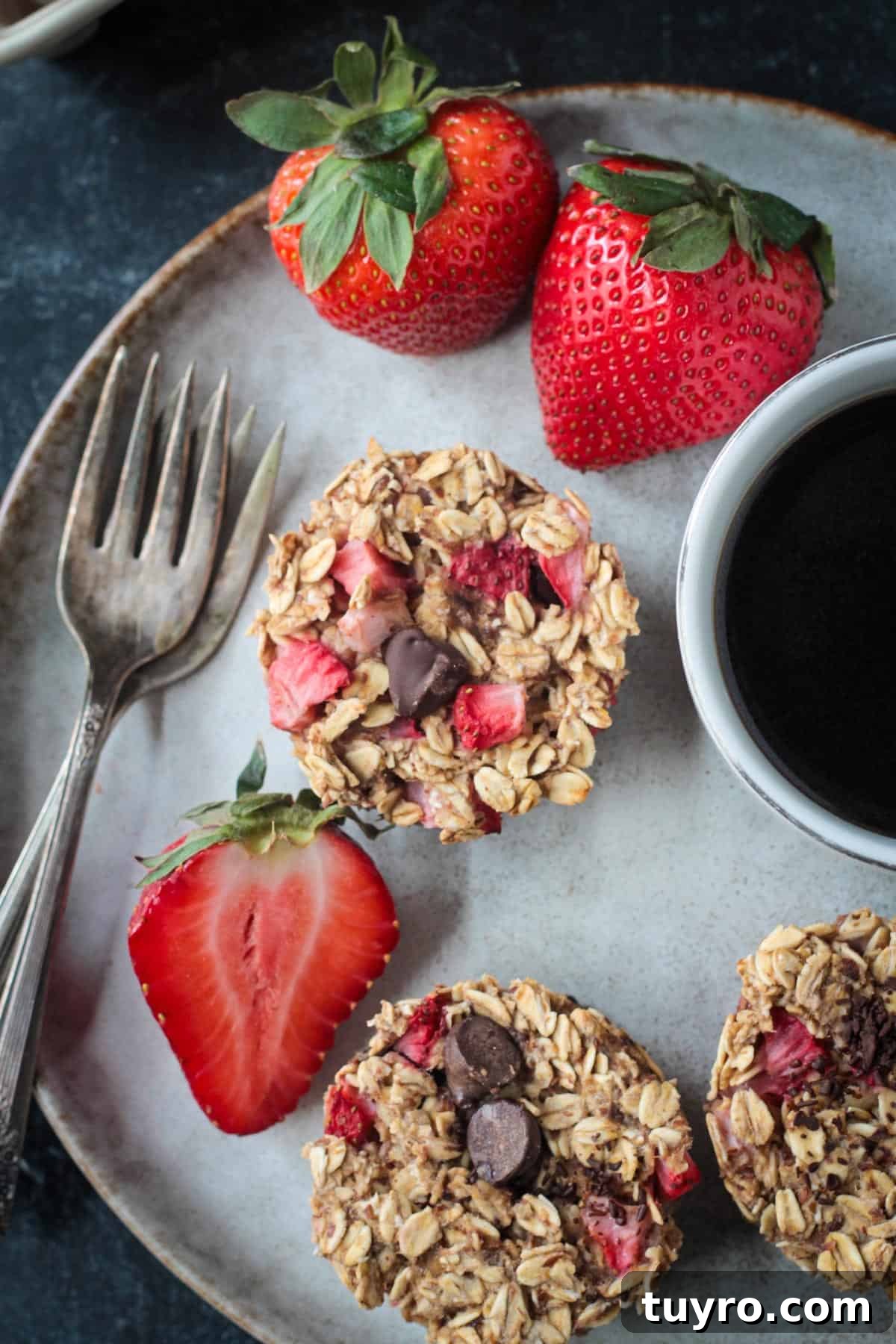 Strawberry Baked Oatmeal Muffins Recipe for Moist Breakfast Bites 11 Overhead view of three strawberry baked oatmeal muffins on a plate with fresh strawberries and two forks.