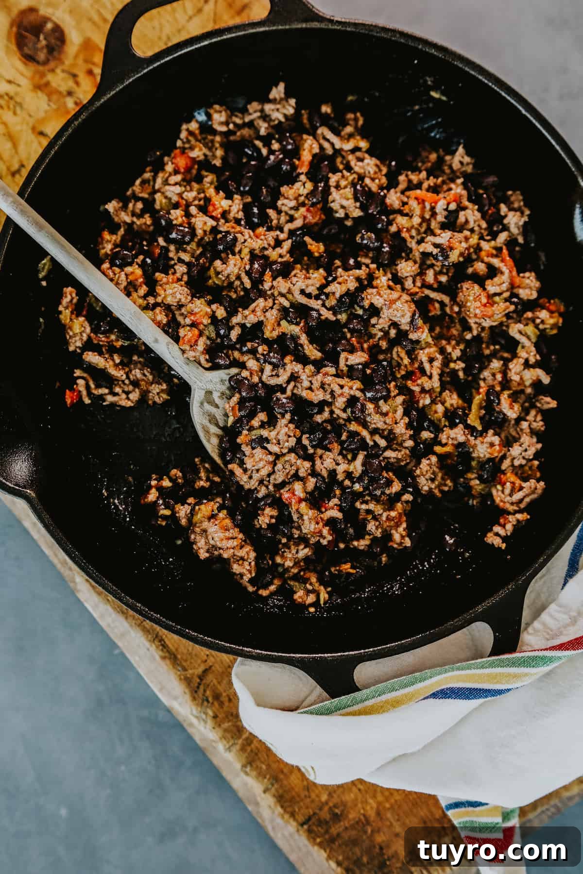 Loaded Oven Baked Beef Nachos with Melted Cheese 3 ground beef and black bean nacho topping mixture in a cast iron skillet.