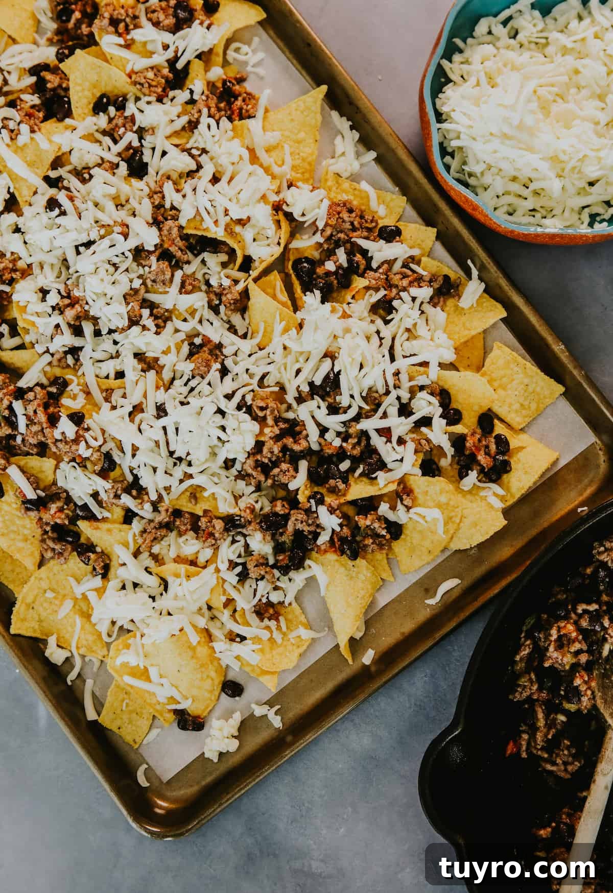 Loaded Oven Baked Beef Nachos with Melted Cheese 4 first layer of nacho tortilla chips on a parchment lined sheet pan topped with the black bean and beef mixture and sprinkled with shredded cheese before baking.