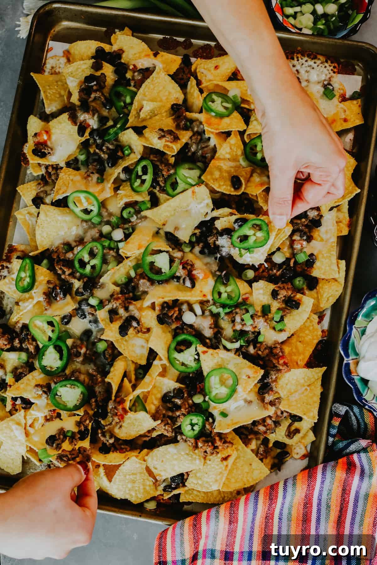 Loaded Oven Baked Beef Nachos with Melted Cheese 5 hands pulling baked beef nachos from the sheet pan.