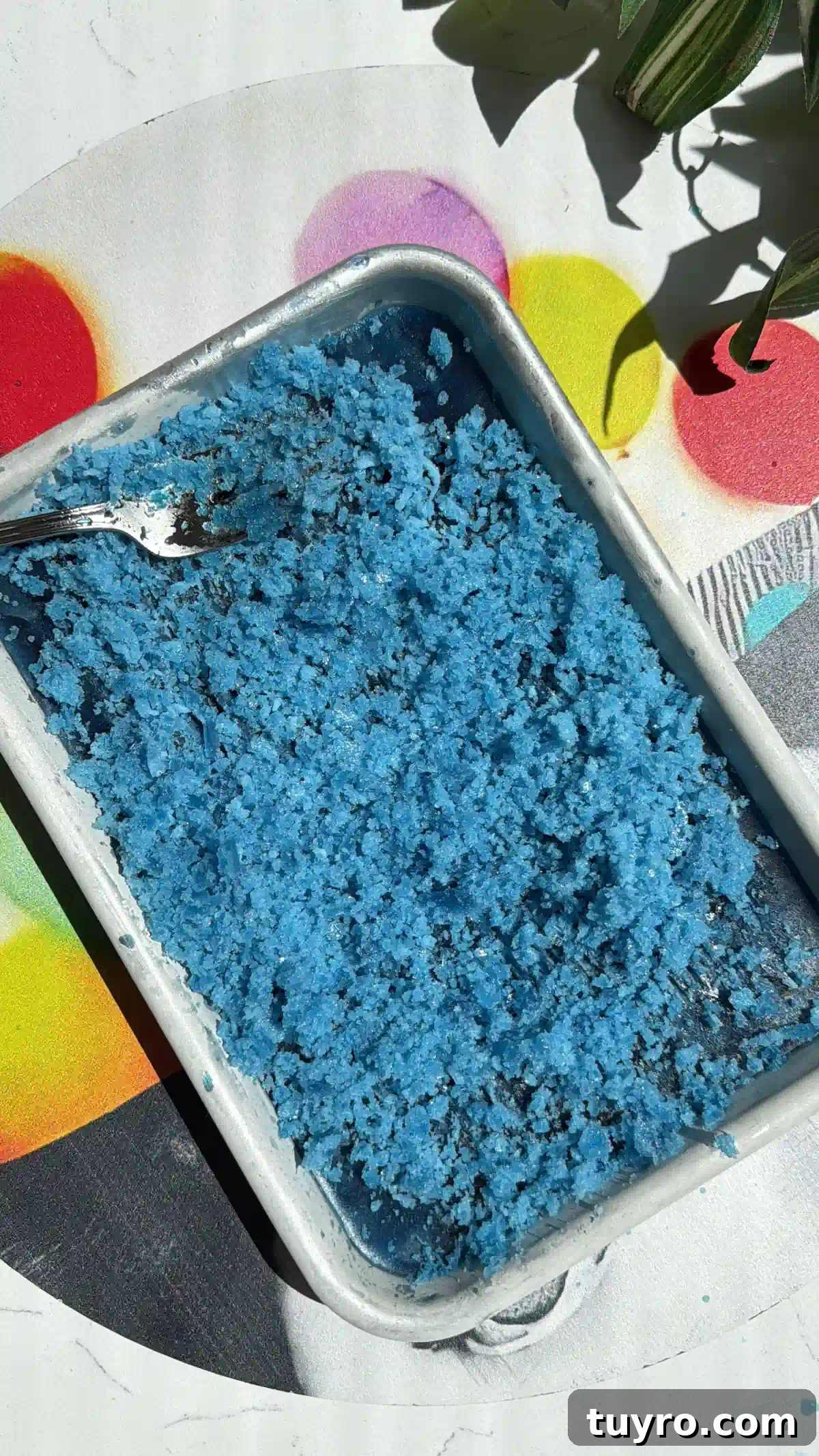Galaxy Cotton Candy Lemonade Cocktail — Color-Changing Drink Tutorial 3 A rectangular metal pan filled with bright blue, scraped butterfly pea granita with a fork resting inside.