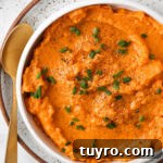 Vegan sweet potato mash in a bowl with fresh green herbs and a gold spoon.