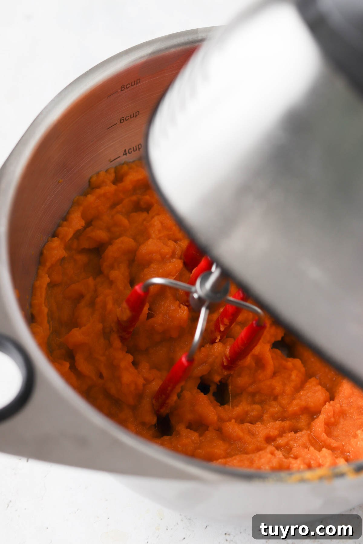 Sweet potato mash in a bowl with a hand mixer resting inside.