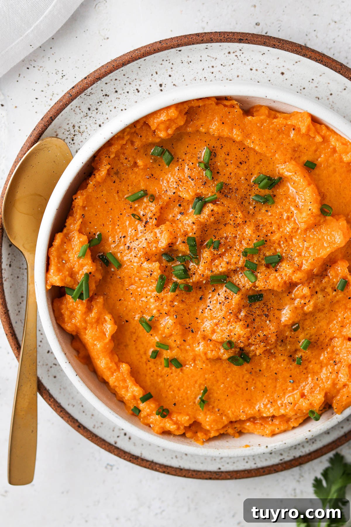 Vegan sweet potato mash in a bowl with fresh green herb garnish and a gold spoon.