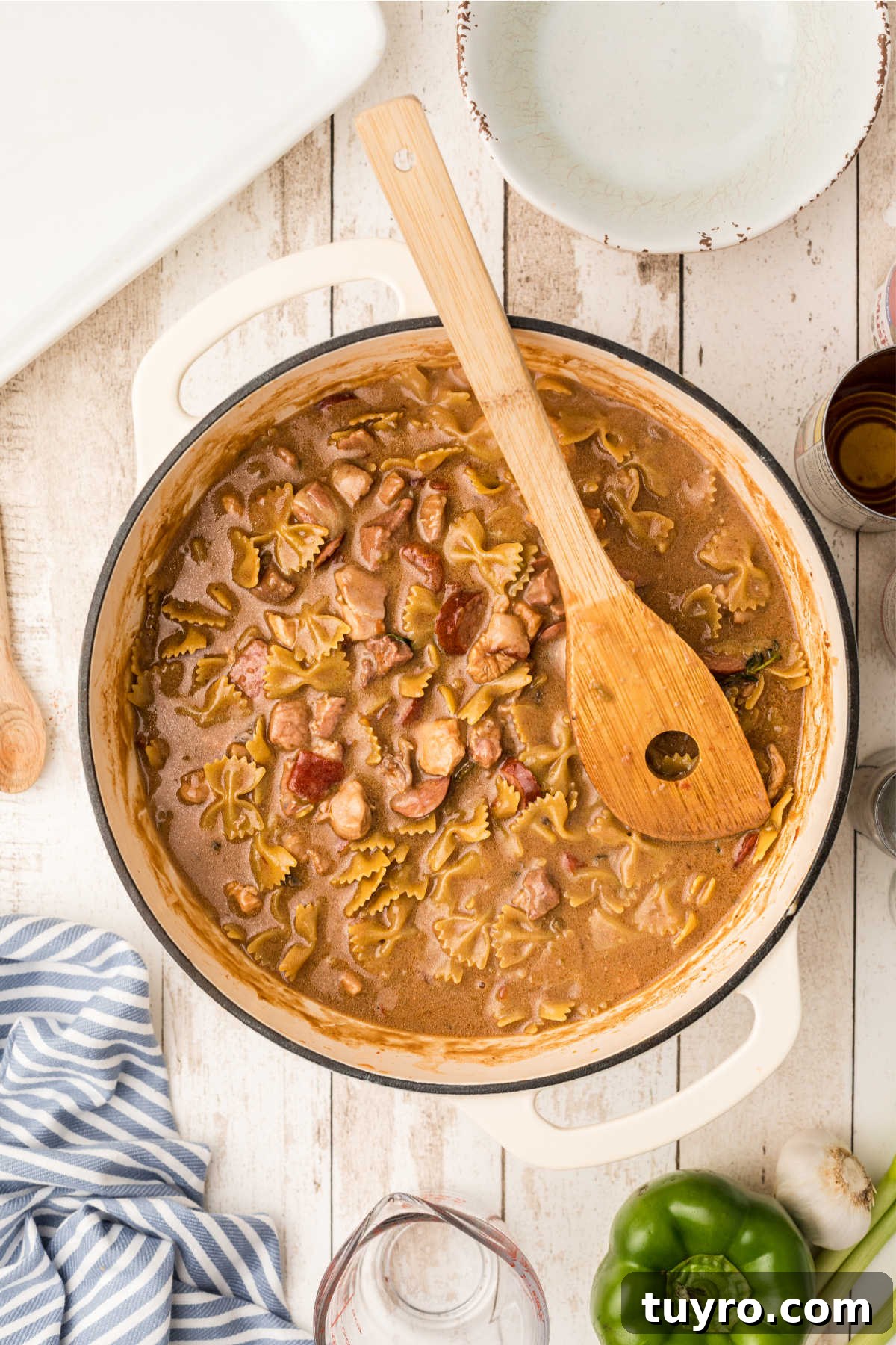 A spatula pushing down ingredients in a Dutch oven, cooking a pastalaya recipe.