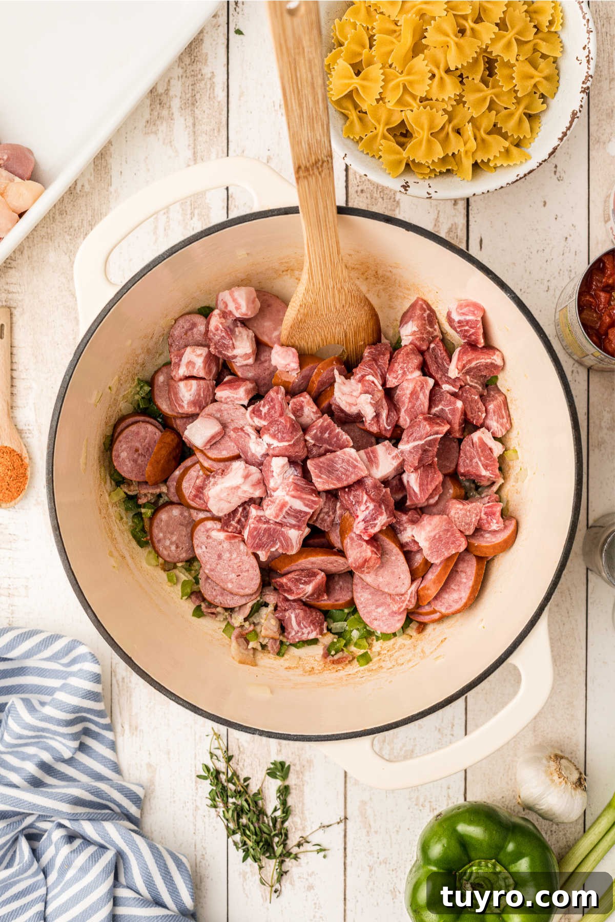 Chopped pork and sausage being added to a Dutch oven with other ingredients.