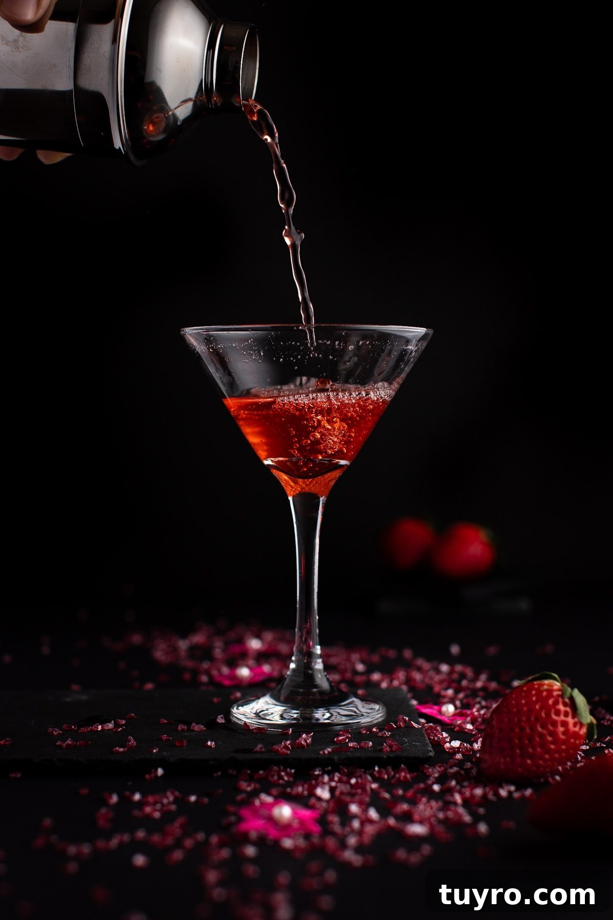 Strawberry martini being poured from a cocktail shaker into a martini glass, on a black background.
