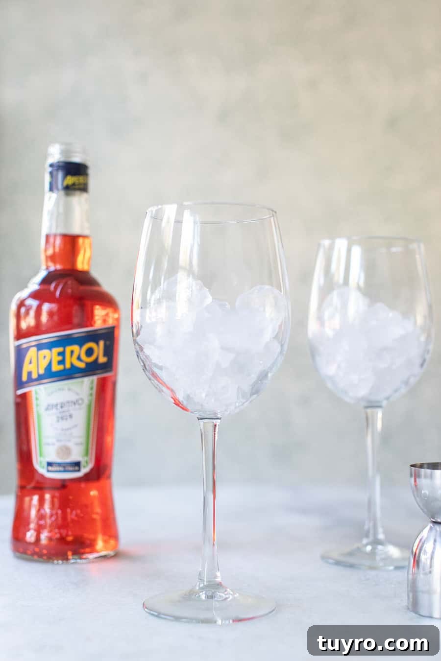 3-Ingredient Aperol Spritz Recipe for Summer Cocktails 3 Wine glass filled with ice and a bottle of Aperol.
