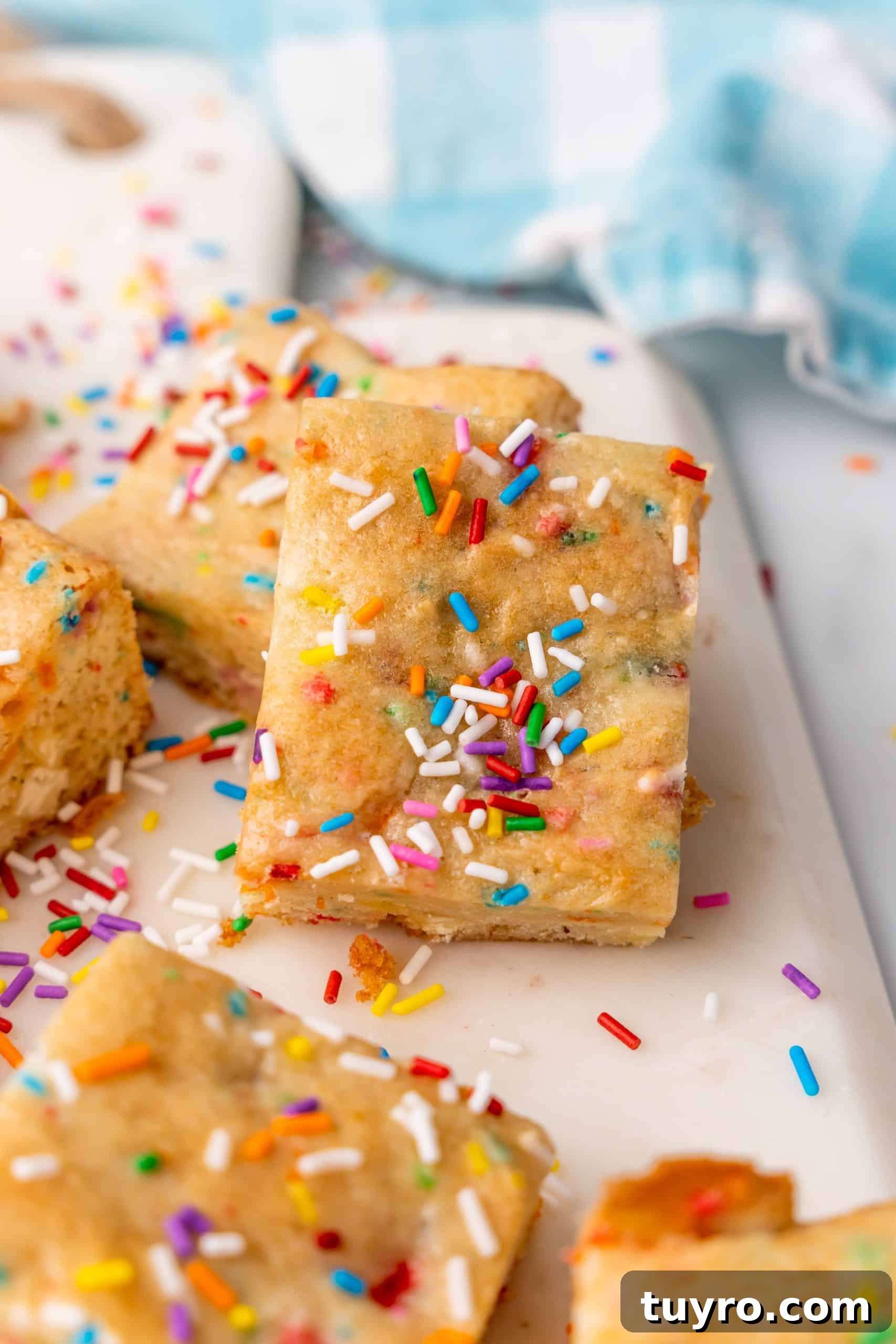 Birthday Cake Blondies Recipe with Sprinkles and Frosting 2 sprinkle topped birthday cake blondies on a white cutting board