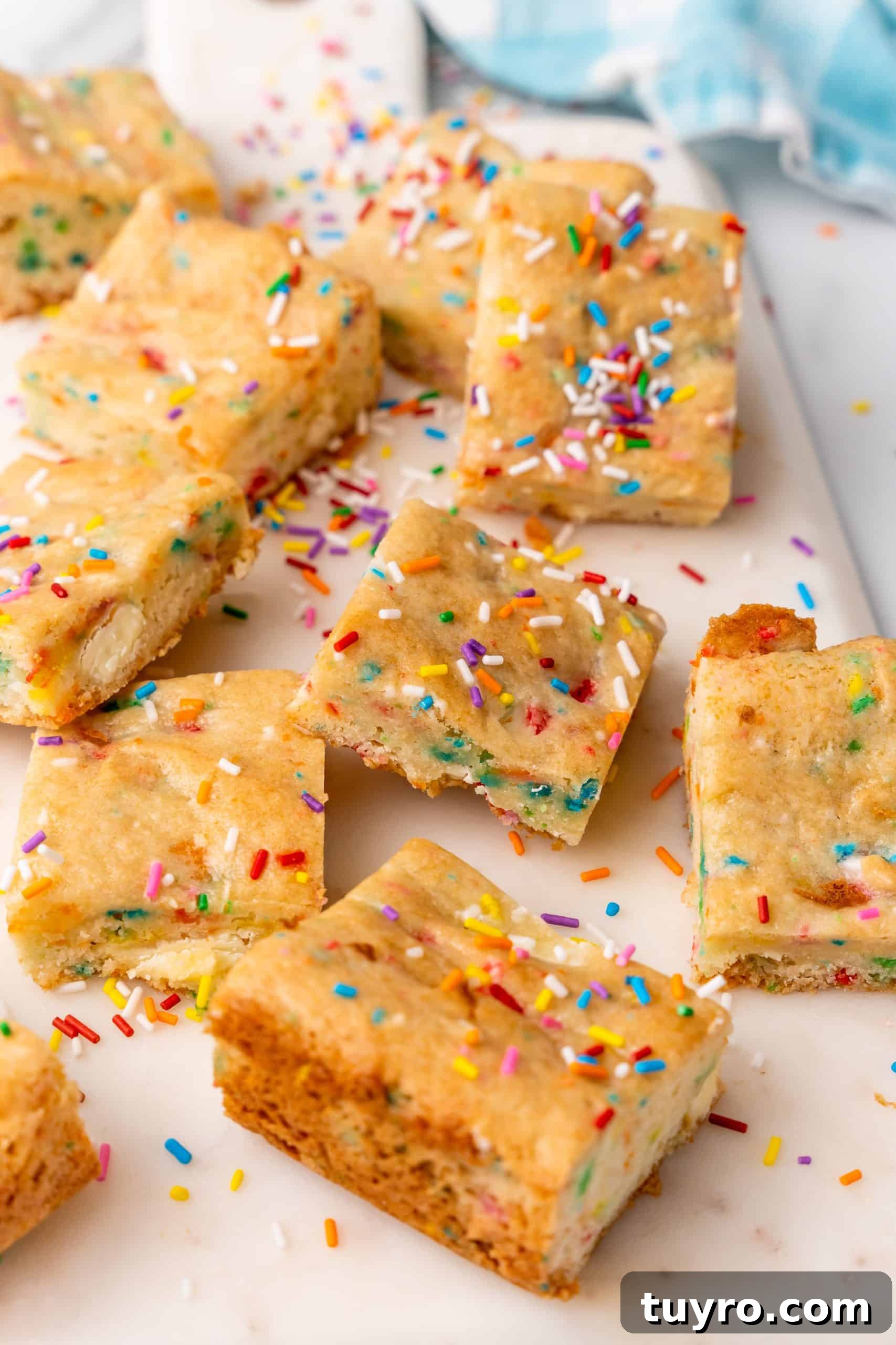 Birthday Cake Blondies Recipe with Sprinkles and Frosting 11 cake batter blondies on a white cutting board