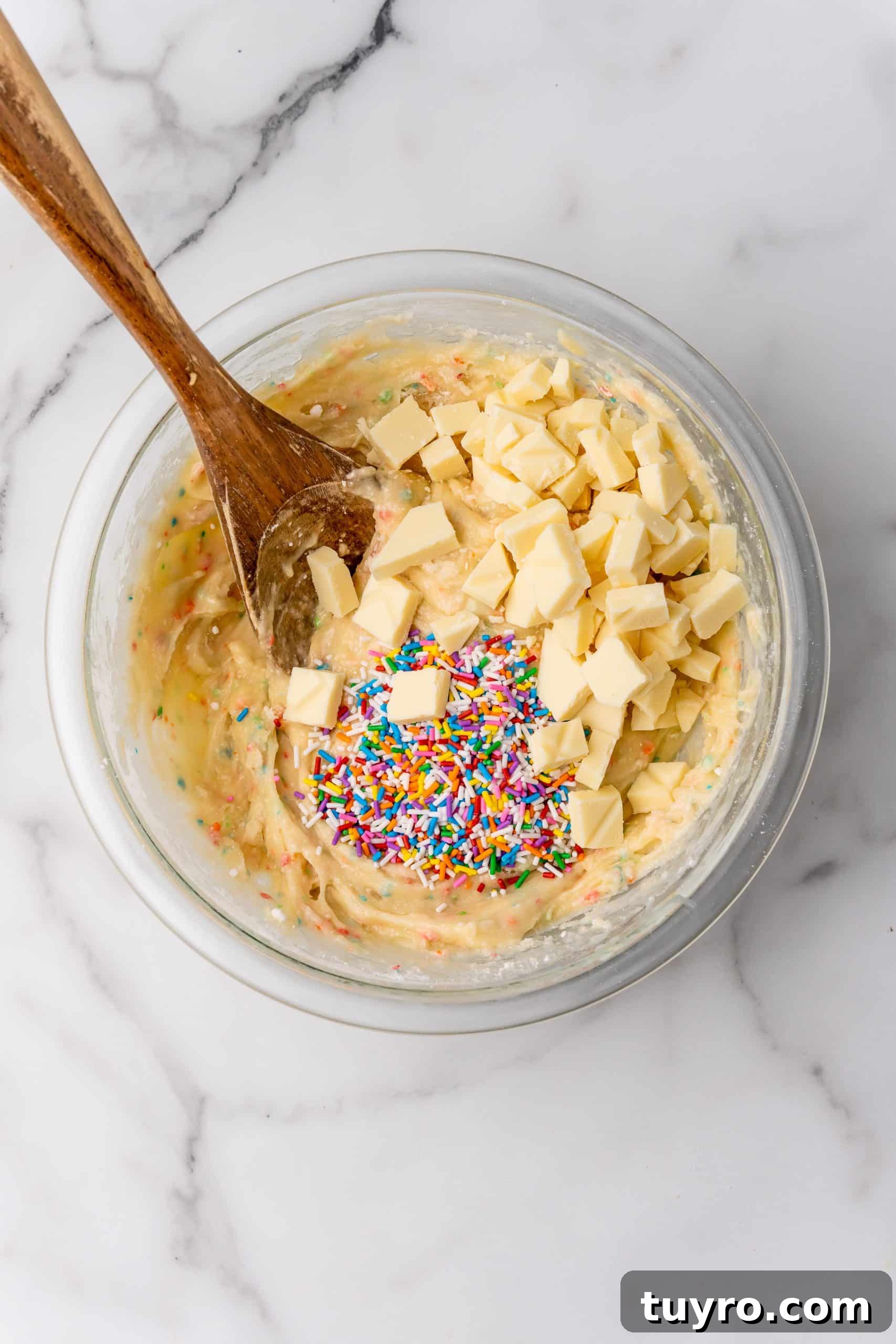 Birthday Cake Blondies Recipe with Sprinkles and Frosting 7 chunks of white chocolate and sprinkles in a glass bowl filled with cake batter