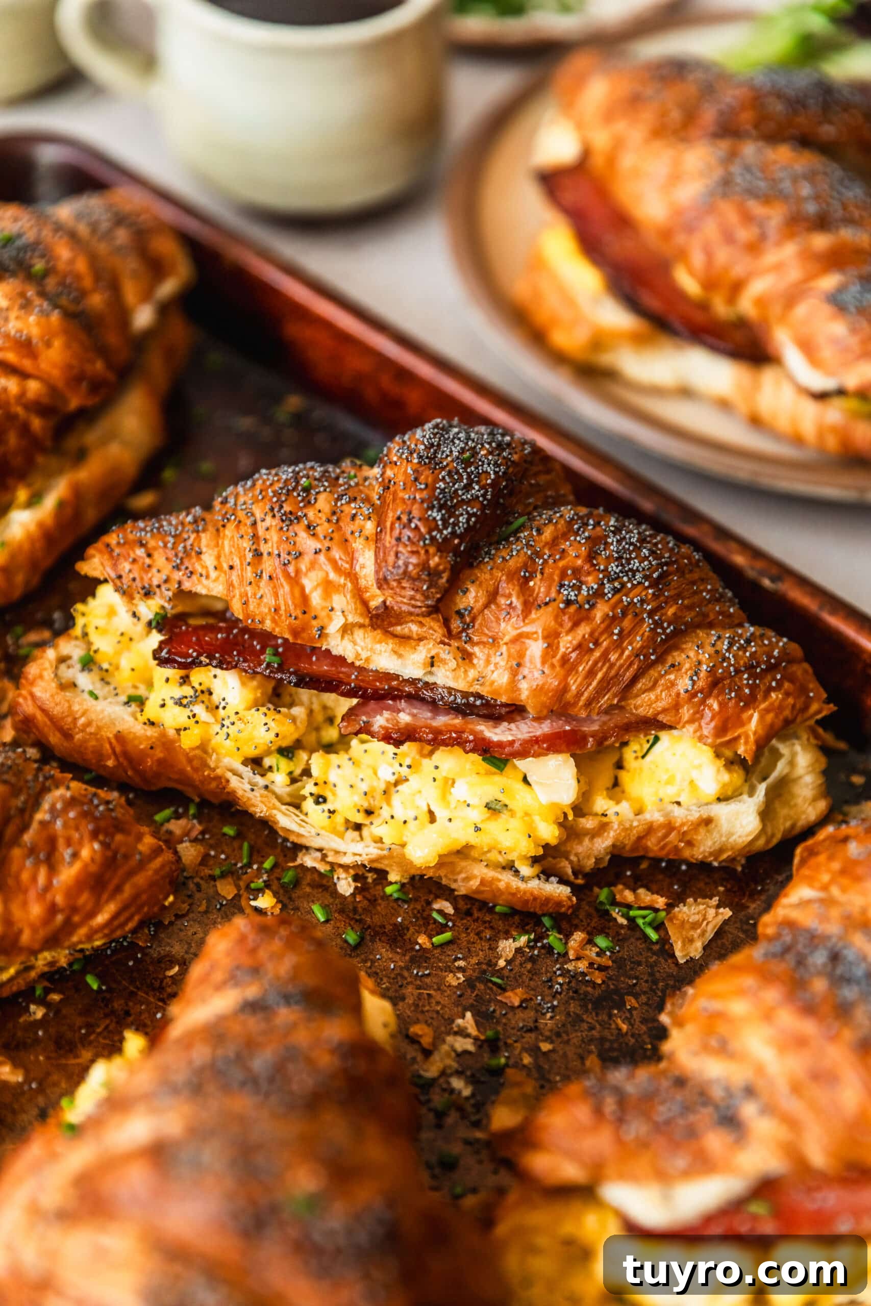 Sheet Pan Bacon, Egg & Cheese Croissant Sandwiches for Brunch 9 A sheet pan of croissant breakfast sandwiches on a countertop next to a plate and coffee.