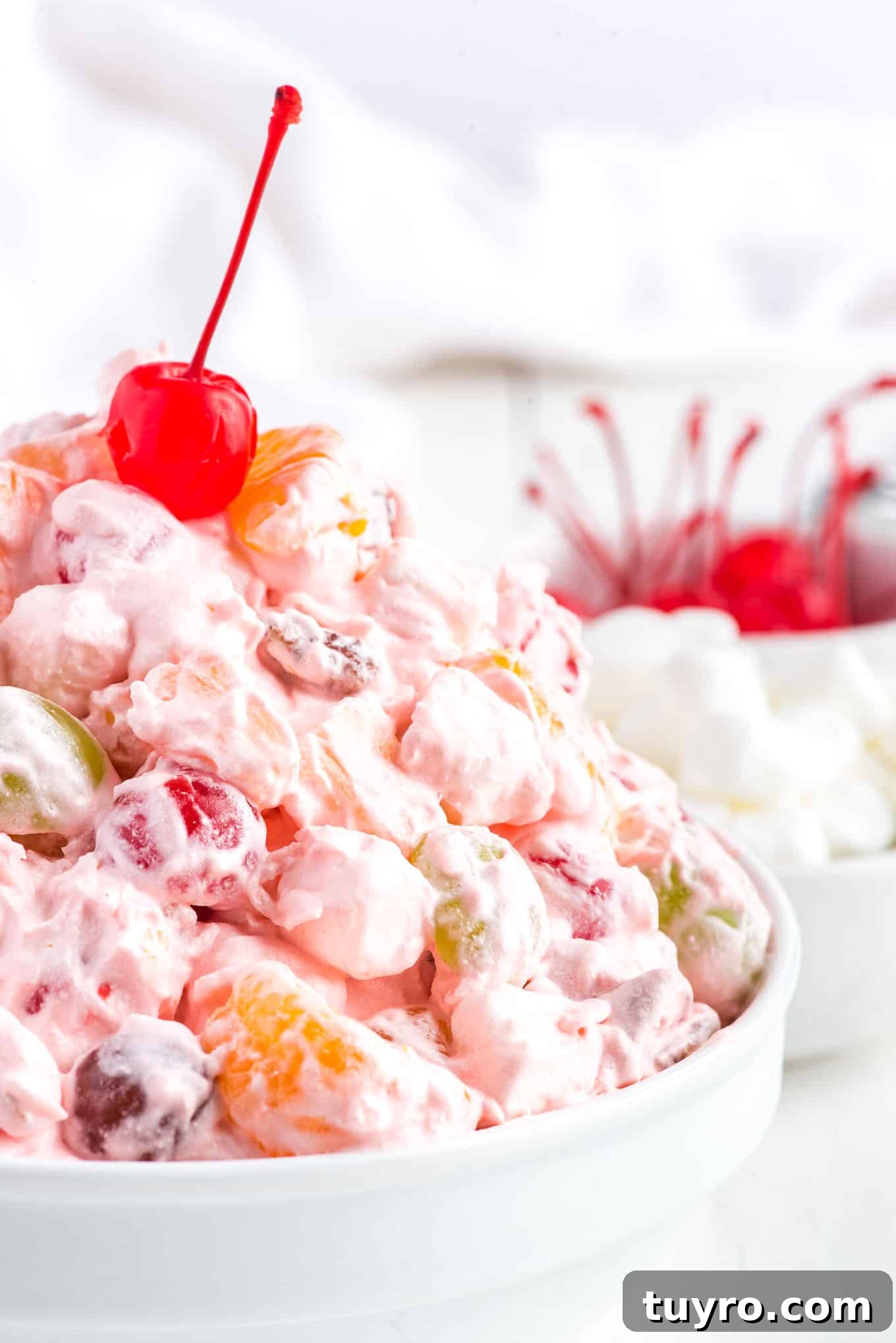 Creamy Fruit Salad with Whipped Topping for Parties 2 A bowl of fruit salad with Cool Whip on the table in front of a bowl of marshmallows.