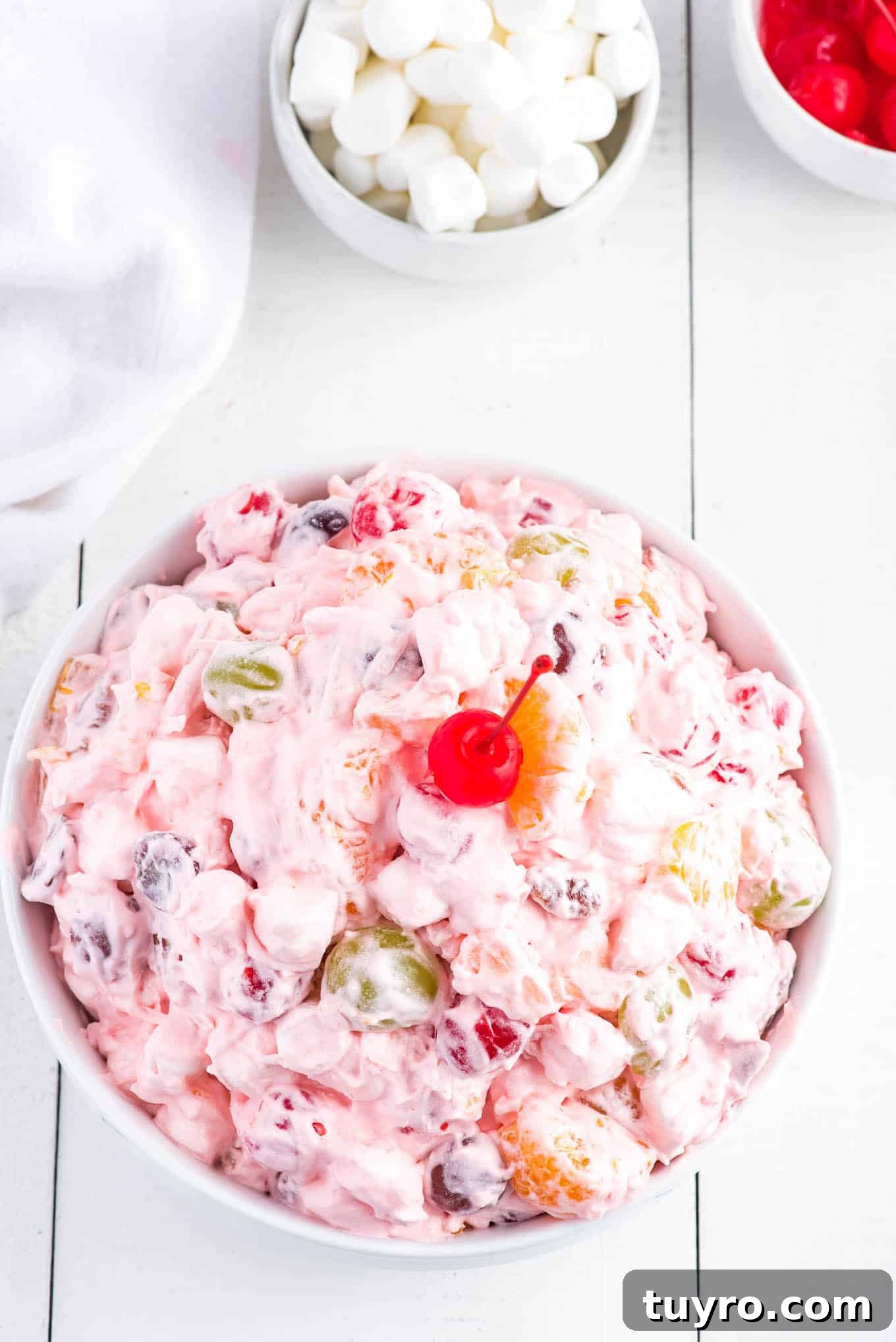 Creamy Fruit Salad with Whipped Topping for Parties 6 Fruit salad with Cool Whip in a bowl garnished with a maraschino cherry.