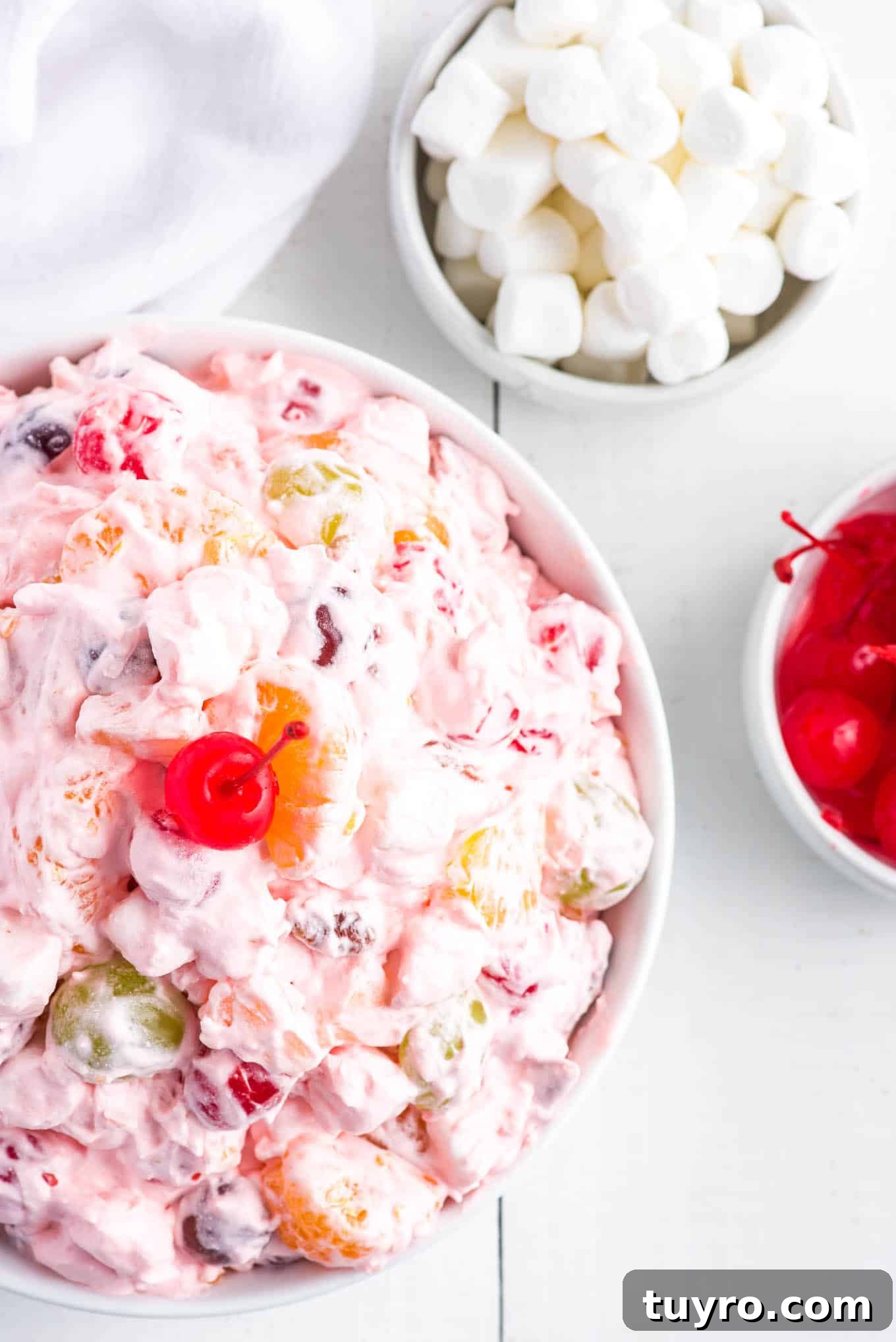 Creamy Fruit Salad with Whipped Topping for Parties 7 Fruit salad with marshmallows and cool whip on the table with a bowl of marshmallows and cherries.