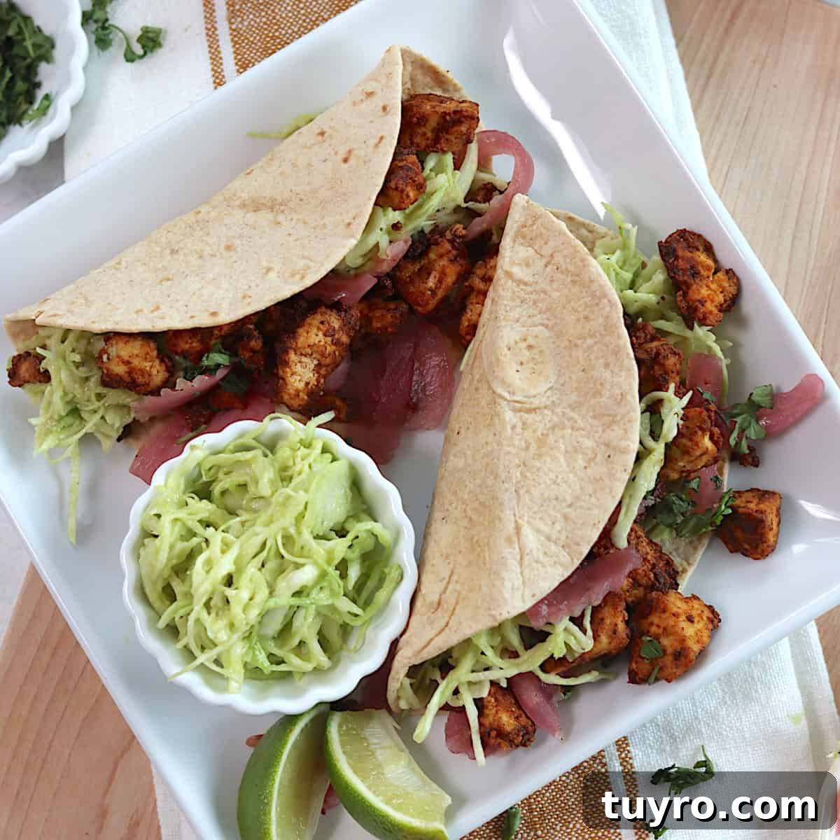 30 Taco Tuesday Ideas for a Craveworthy Dinner 13 Two tofu tacos on a white square plate with two lime wedges and a small bowl of slaw on the plate.
