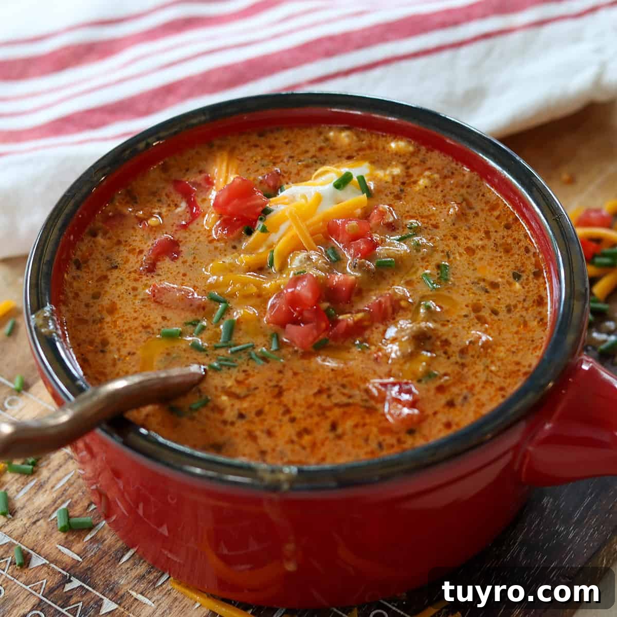 30 Taco Tuesday Ideas for a Craveworthy Dinner 6 Square side image of soup served in a red bowl on a wooden cutting board. Soup is garnished with sour cream, tomato, green onion, and cheddar cheese. A spoon is ready for you to take a bite.