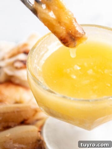 A piece of crab meat being dunked into a bowl of butter.