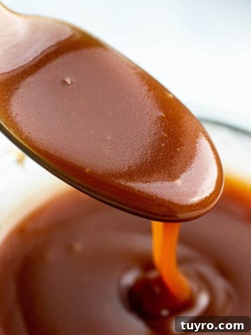 A spoon scooping out some caramel sauce out of a glass jar