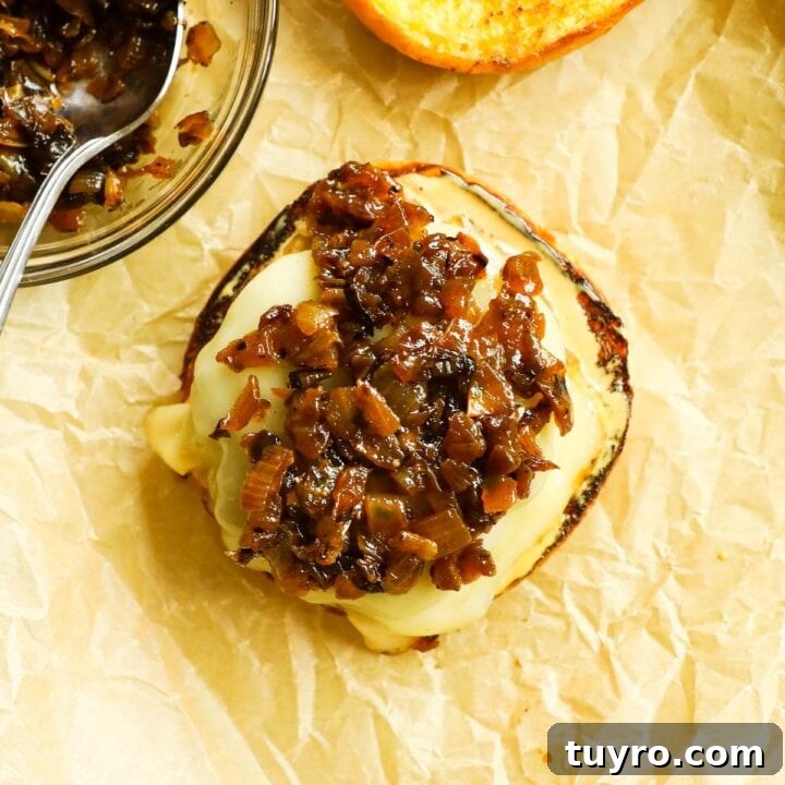 Burger topped with caramelized onions on a baking sheet with parchment paper.