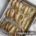 Roasted caramelized shallots on a baking sheet with dried herbs.