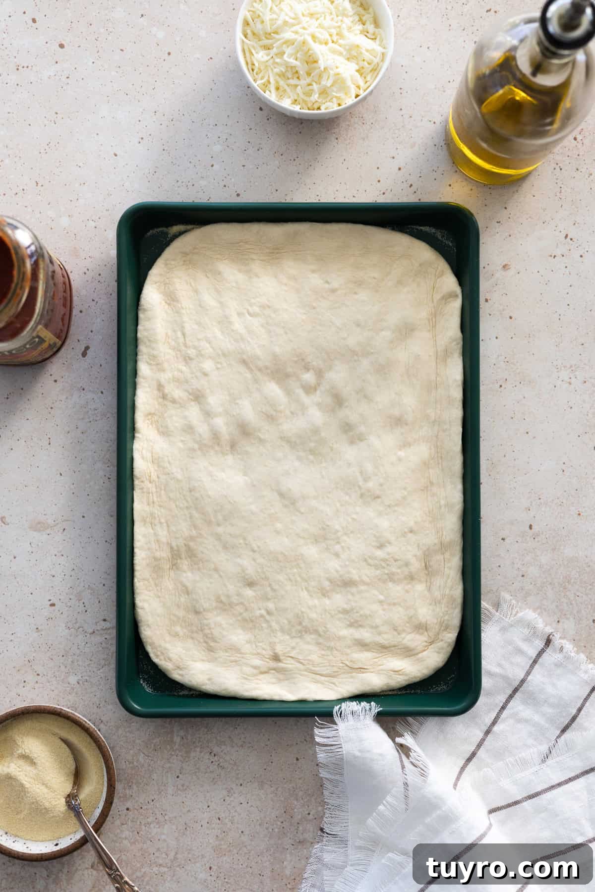 Sourdough Discard Pizza Dough flattened on a green baking sheet. 