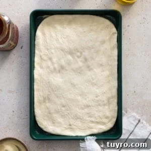 Sourdough discard pizza dough shaped on a green baking sheet.