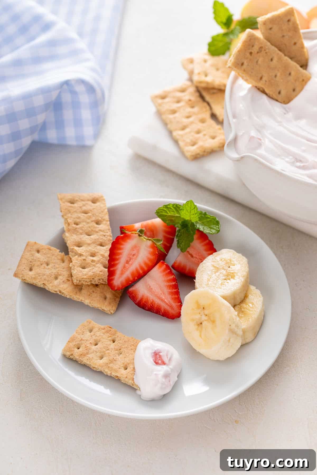 Yogurt fruit dip, graham crackers, fresh strawberries and banana slices on a white plate.