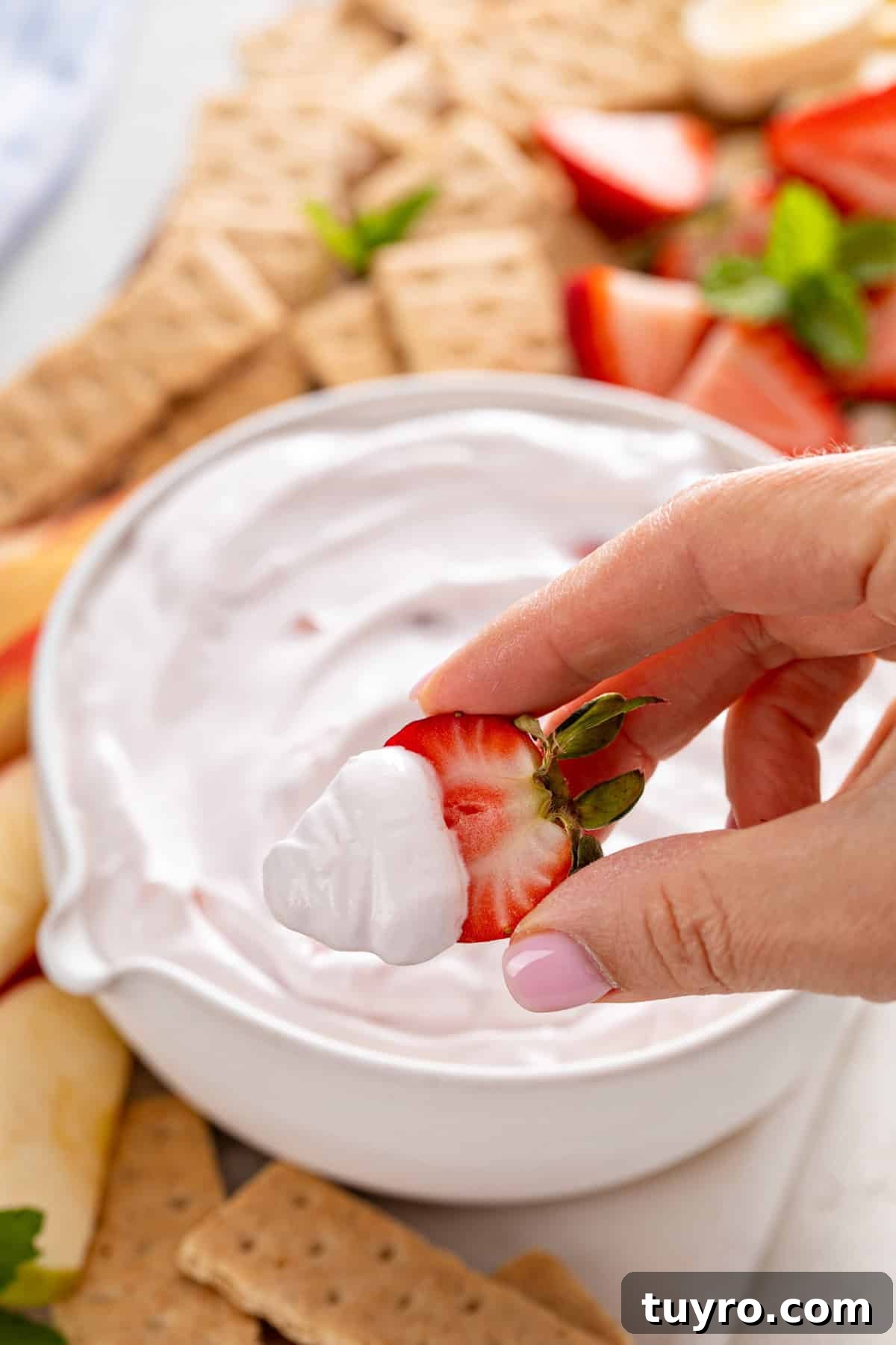 Hand holding up a halved fresh strawberry that's been dipped in yogurt fruit dip.