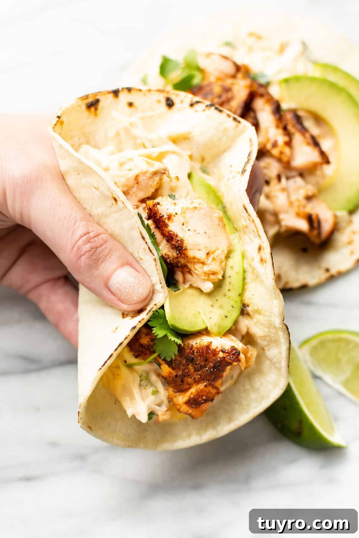 Grilled Salmon Tacos with Avocado Lime Crema 6 a hand holding a salmon taco