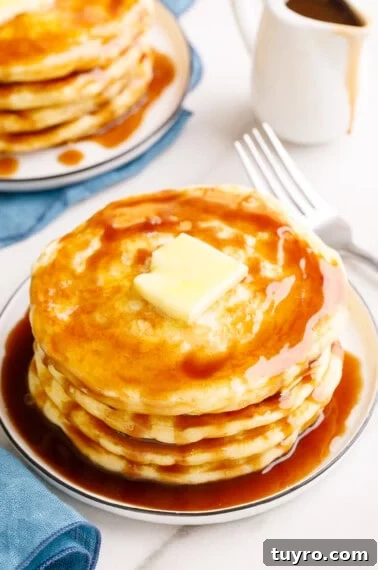 Fluffy Homemade Strawberry Waffles Recipe 11 A stack of overnight pancakes on a plate topped with butter and syrup.