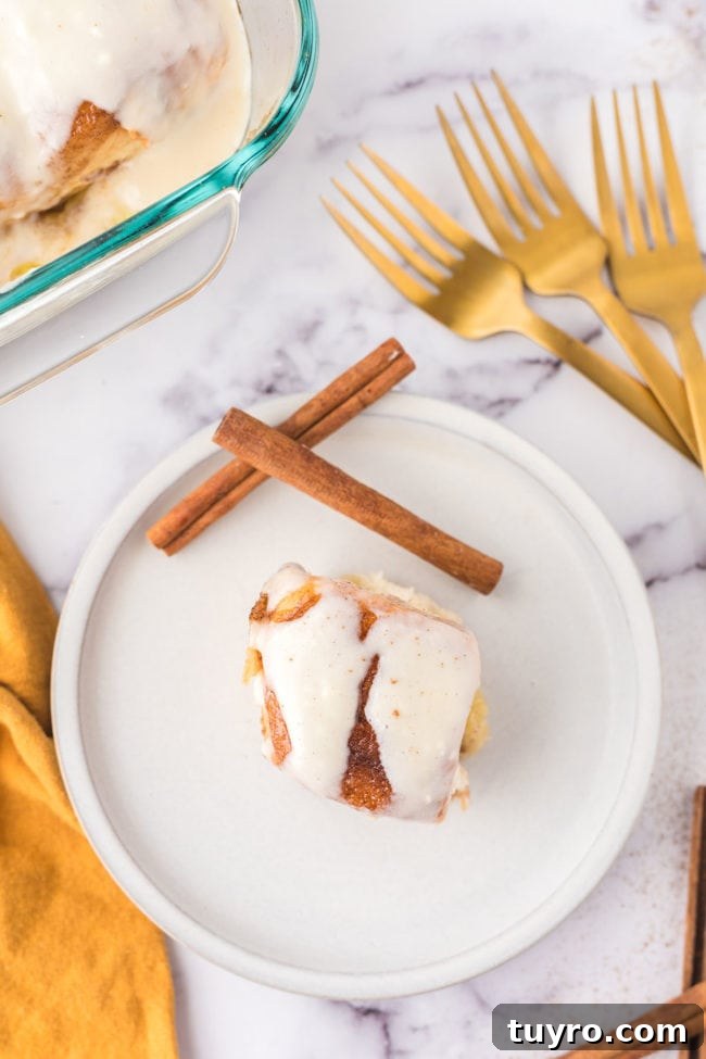 30-Minute Homemade Cinnamon Rolls 9 homemade cinnamon roll on a plate with 2 cinnamon sticks and gold forks on the table next to the plate.