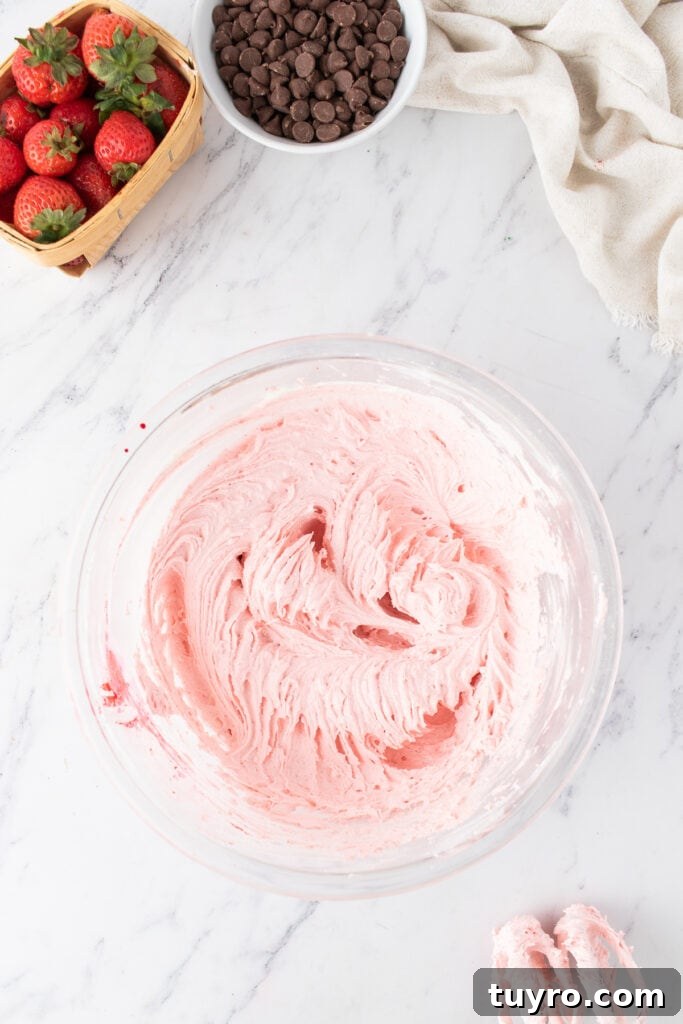 Chocolate Strawberry Cake with Rich Ganache 7 Bowl of fluffy pink strawberry buttercream frosting with a hand mixer and fresh strawberries nearby.