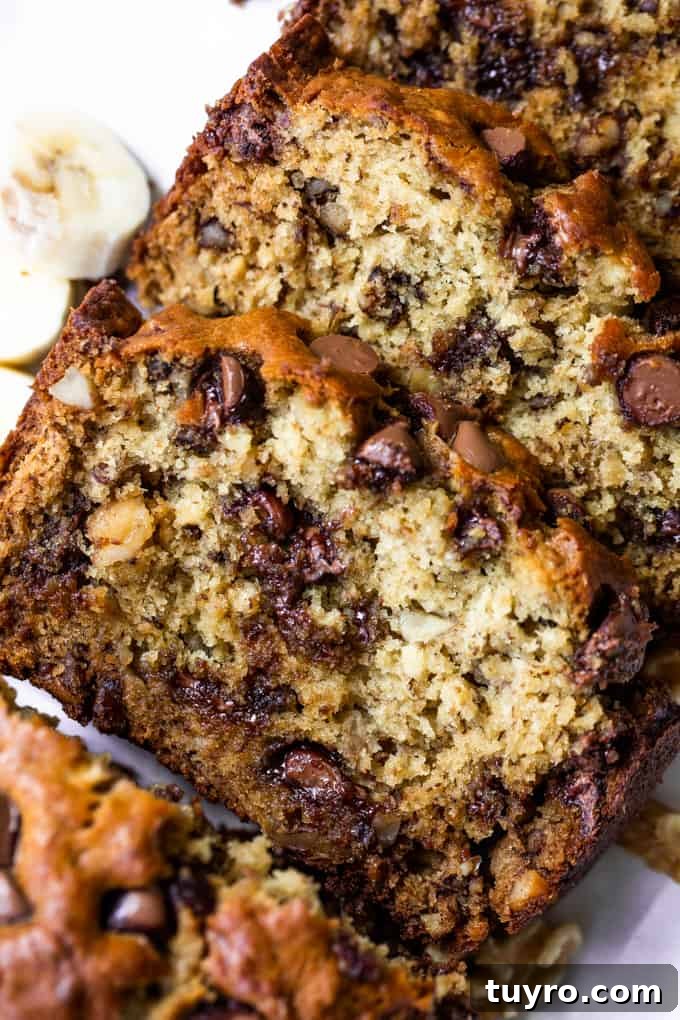 Sliced loaf of chunky monkey banana bread showing banana bread with chunks of walnut, and melted chocolate chips. Slices of bananas and walnuts on the side.