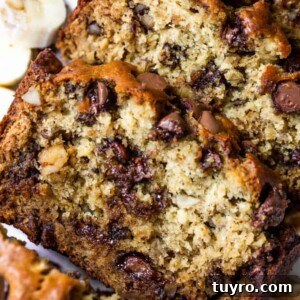 Sliced loaf of chunky monkey banana bread showing banana bread with chunks of walnut, and melted chocolate chips. Slices of bananas and walnuts on the side.