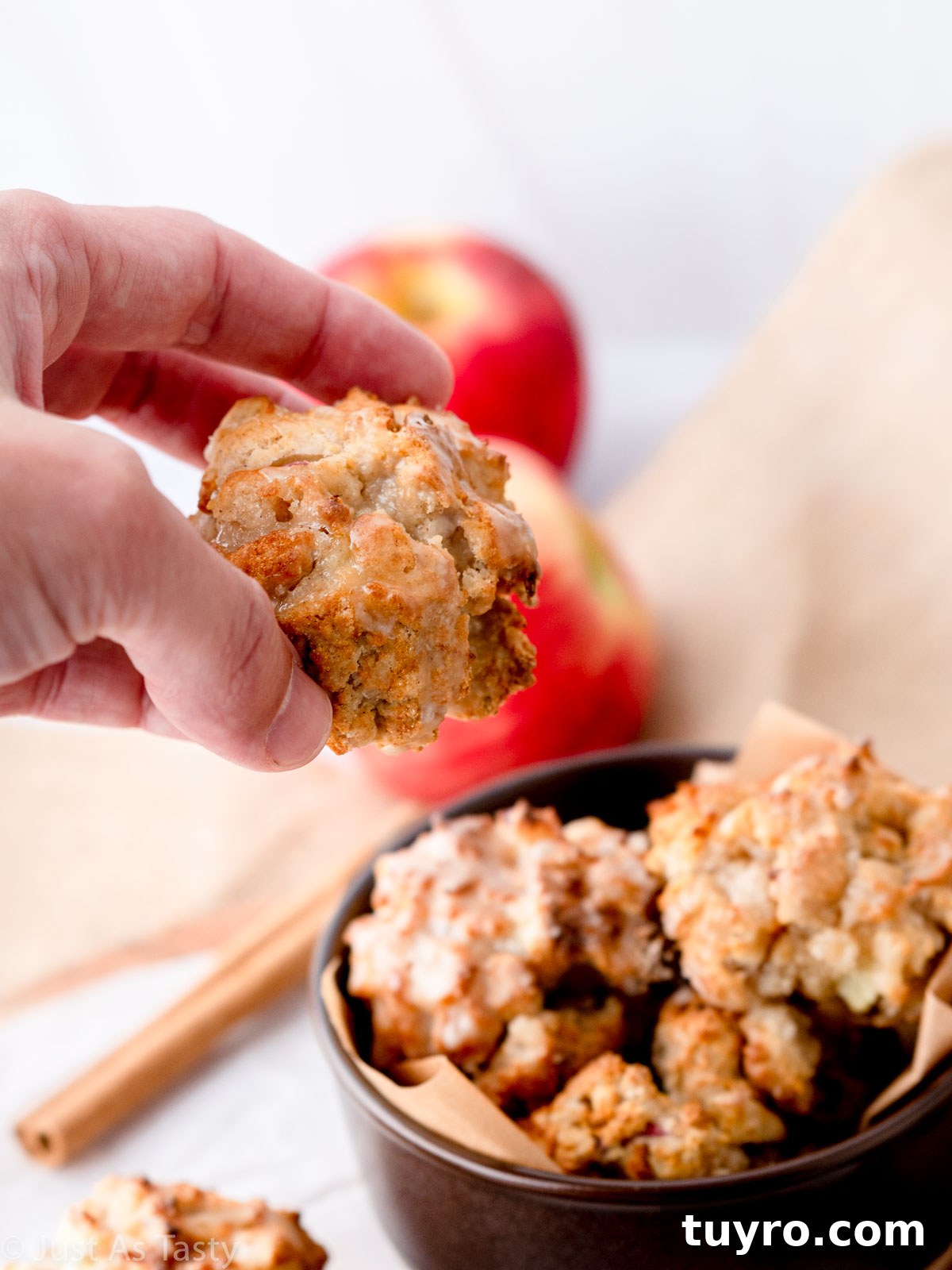 Crispy Air Fryer Apple Fritters Recipe 3 Hand picking up a glazed apple fritter out of a bowl.