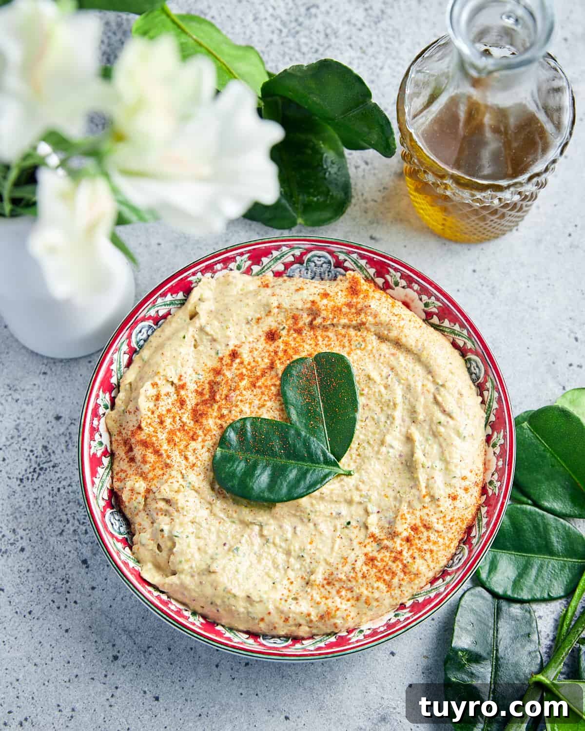 Vegan Whipped Feta Dip with Pistachios Lime Leaves and Rosemary 2 Portrait overhead photo of vegan whipped feta dip with pistachios, served in a pretty dish on a grey background, with lime leaves, flowers and olive oil surrounding.