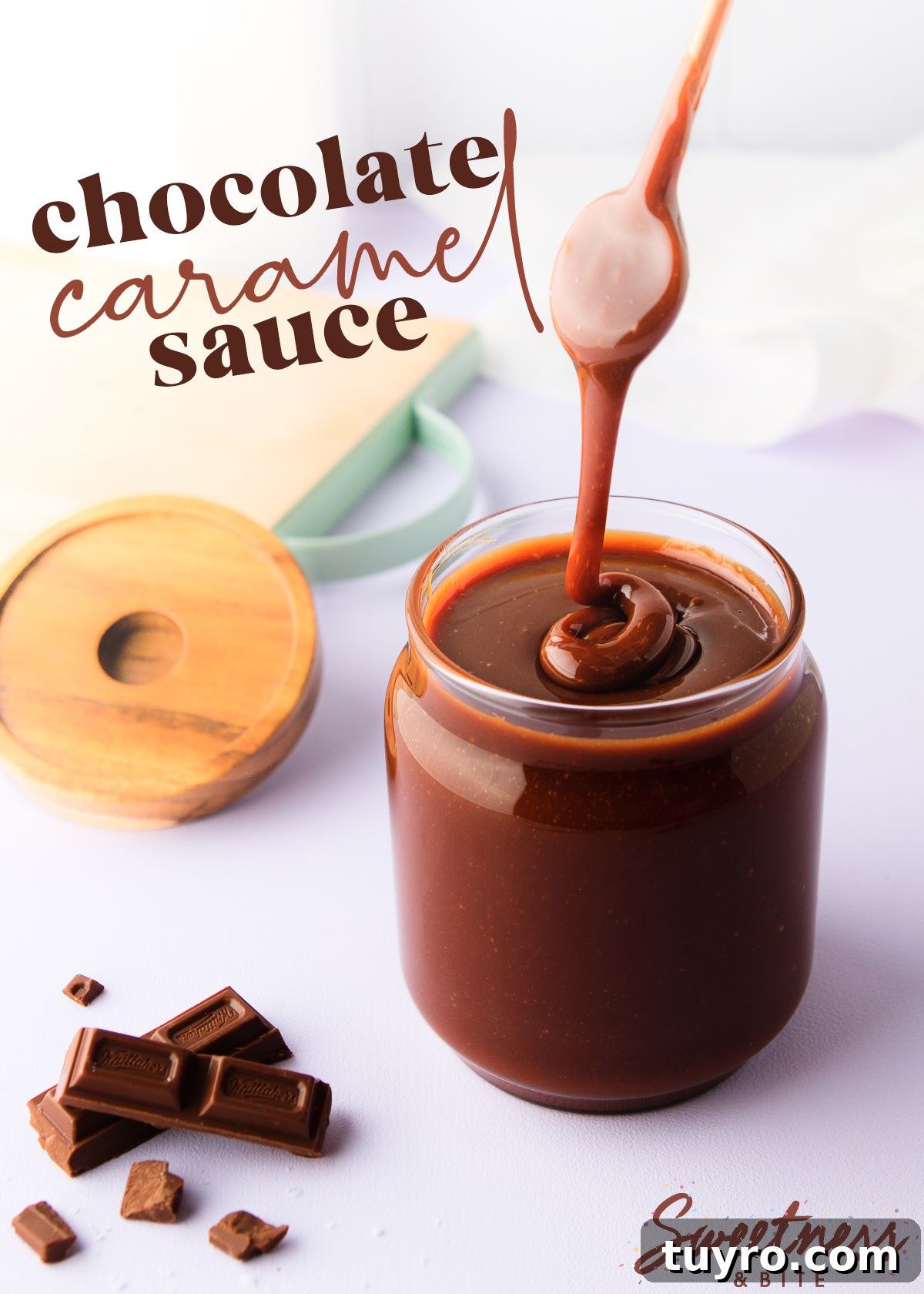 Decadent Chocolate Caramel Sauce Recipe for Desserts 2 A jar of chocolate caramel sauce on a pale purple background, with a spoon drizzling the thick sauce back into the jar, and some chopped chocolate next to the jar.
