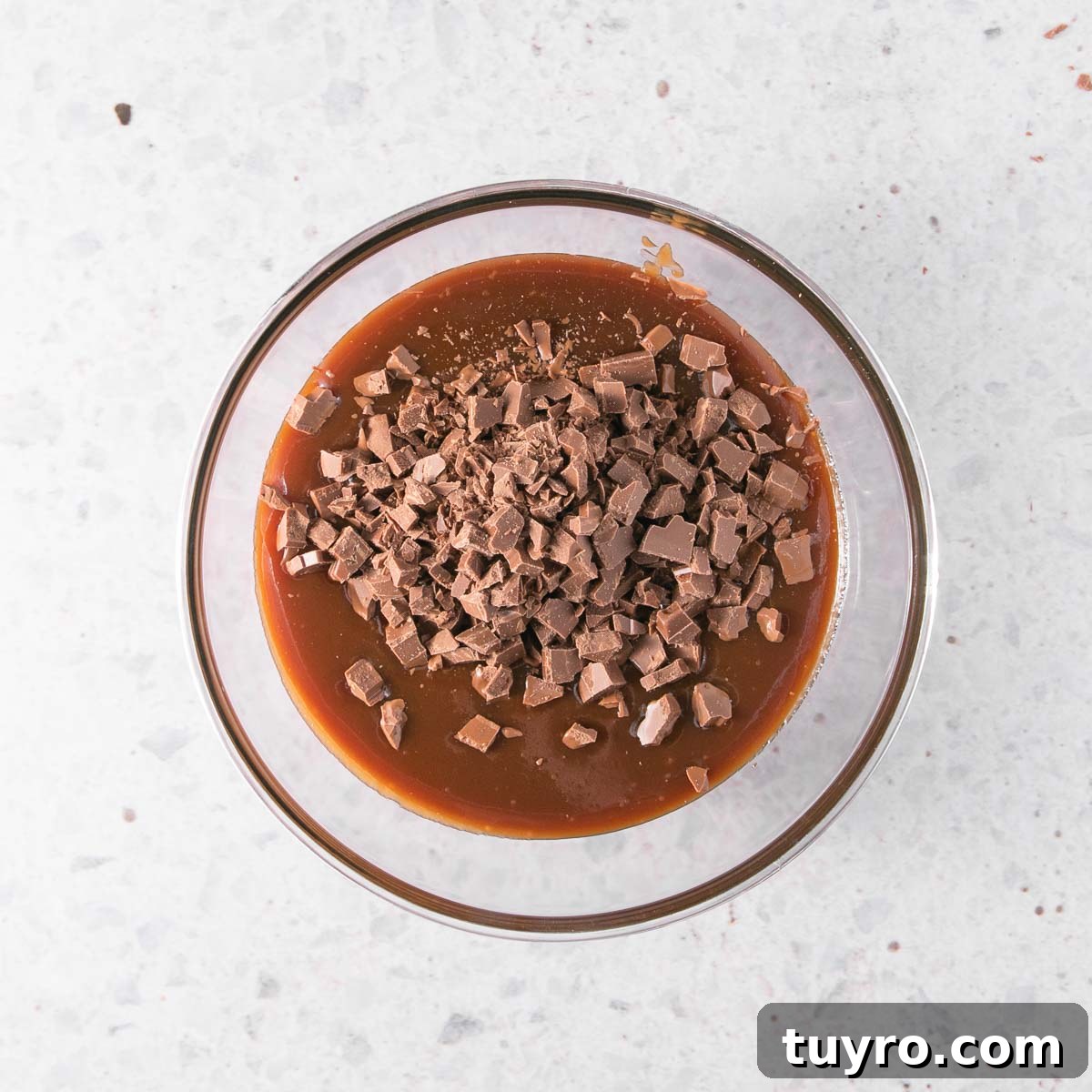 Decadent Chocolate Caramel Sauce Recipe for Desserts 11 The caramel sauce in a glass bowl, with chopped chocolate sitting on top.