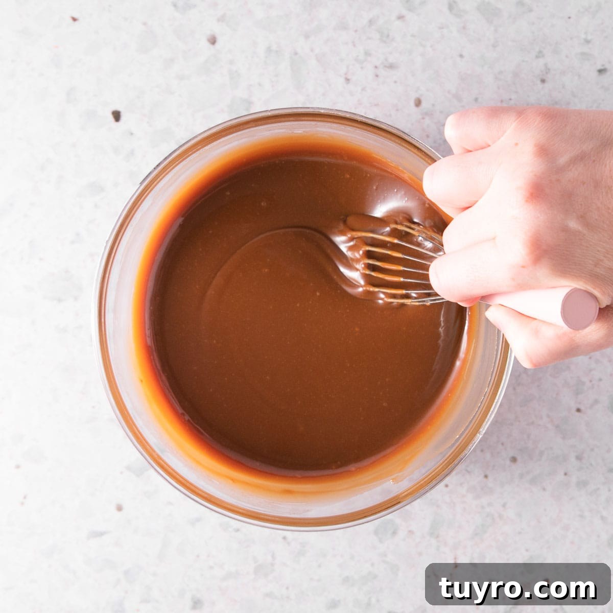 Decadent Chocolate Caramel Sauce Recipe for Desserts 12 A hand stirring the finished sauce with a pink-handled whisk.