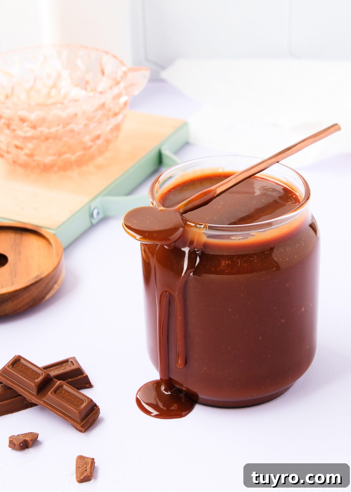 Decadent Chocolate Caramel Sauce Recipe for Desserts 13 The sauce in a glass jar, with a long-handled copped spoon resting on top, and a big drip of sauce dripping from the end of the spoon, down the side of the jar.