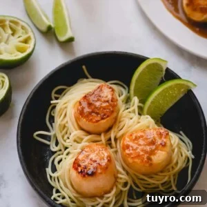 3 seared scallops over a bed of spaghetti and garnished with lime wedges.