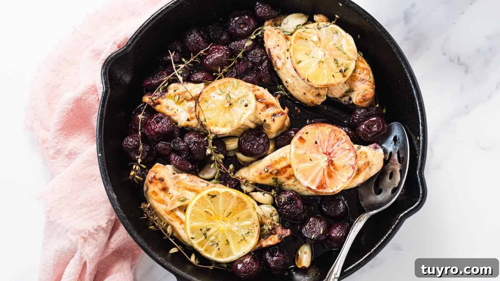 Skillet with roasted chicken breasts, lemon slices, grapes, herbs, and garlic cloves.