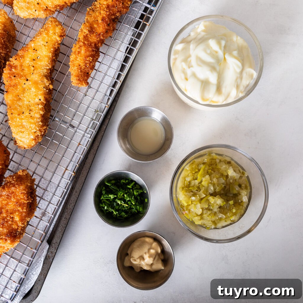 tartar sauce ingredients. bowl of mayonnaise, dill pickle relish, fresh chopped chives, dijon mustard, and lemon juice next to salmon fish sticks on a wire rack