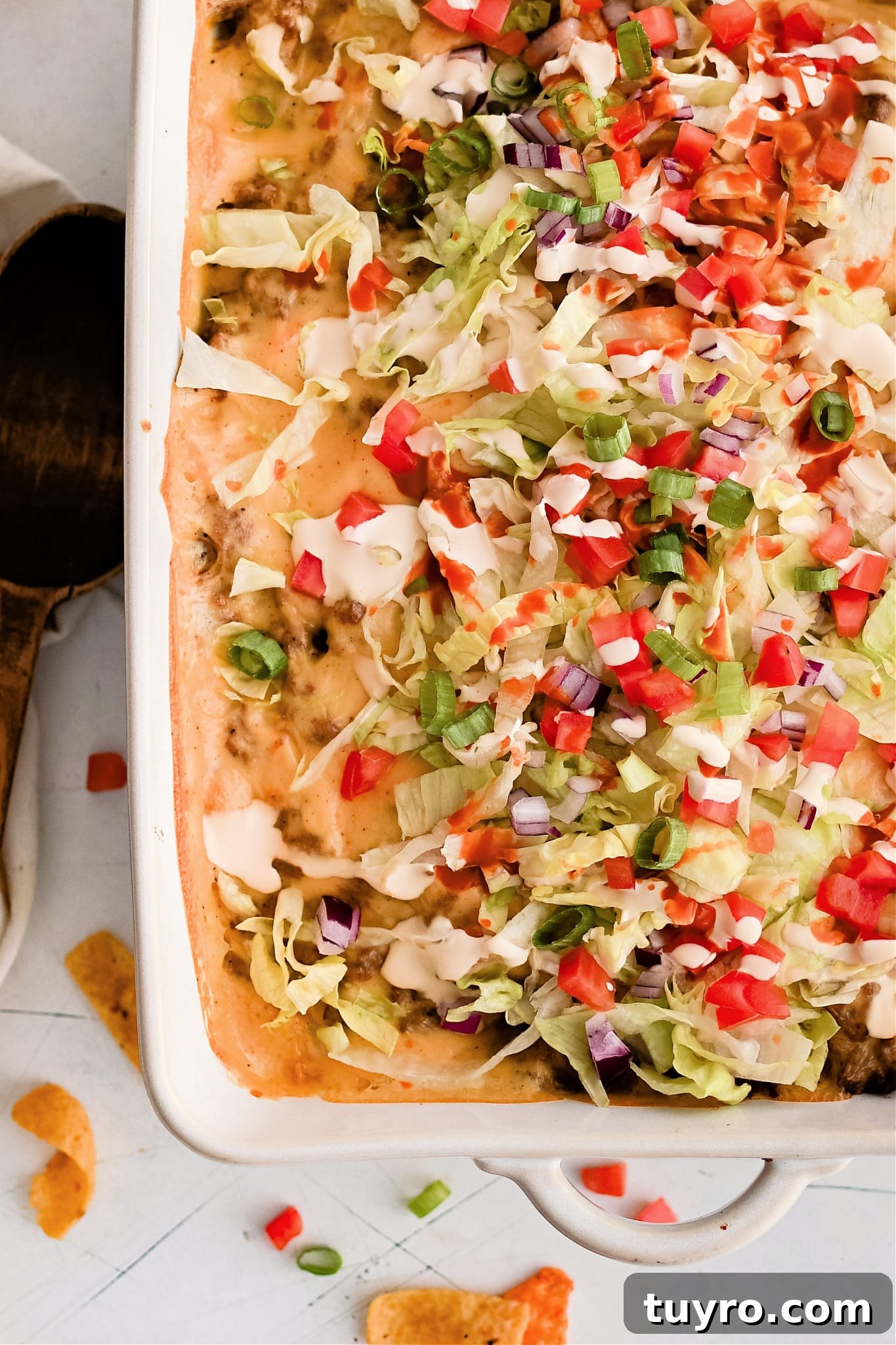 Baked walking taco casserole in a large 9x13-inch baking dish topped with shredded lettuce, tomatoes, sour cream, and hot sauce.